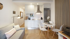 A modern kitchen with white cabinets, a stainless steel range hood, and a built-in oven. There is a dining area with a round table and white chairs. - Apartment 'Bonito Apartamento En Gava Mar' with Private Terrace, Wi-Fi and Air Conditioning (Gavà)