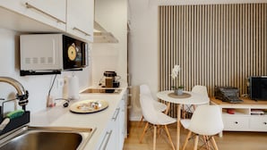 A modern kitchen with a microwave, coffee maker, and dining area with white chairs and a small table. - Apartment 'Bonito Apartamento En Gava Mar' with Private Terrace, Wi-Fi and Air Conditioning (Gavà)