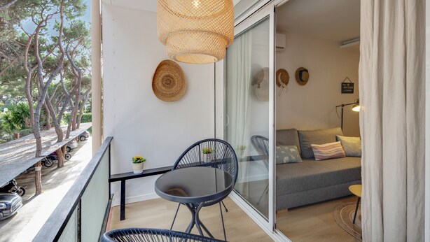 A balcony with a table and chairs, a wicker pendant light, and a view of trees and parked cars. - Apartment 'Bonito Apartamento En Gava Mar' with Private Terrace, Wi-Fi and Air Conditioning (Gavà)