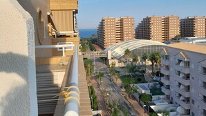 A high-rise building with a curved glass structure, a view of the sea, and multiple residential buildings in the background.
