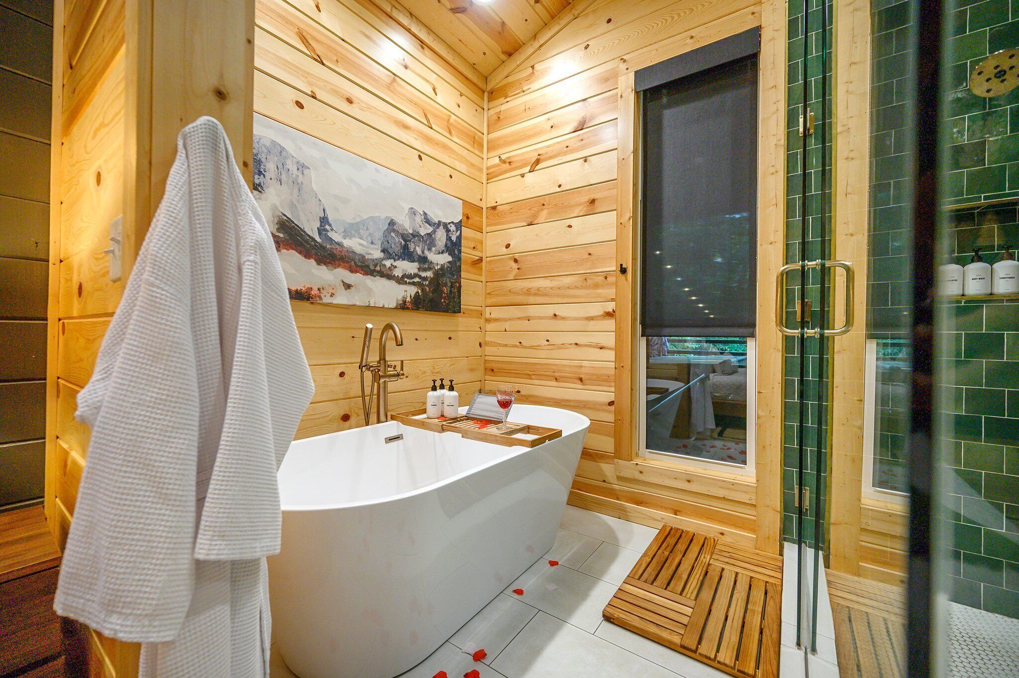 Une salle de bain rustique, avec des murs en bois, comprenant une baignoire sur pieds, une douche en verre et un tableau représentant un paysage de montagne.