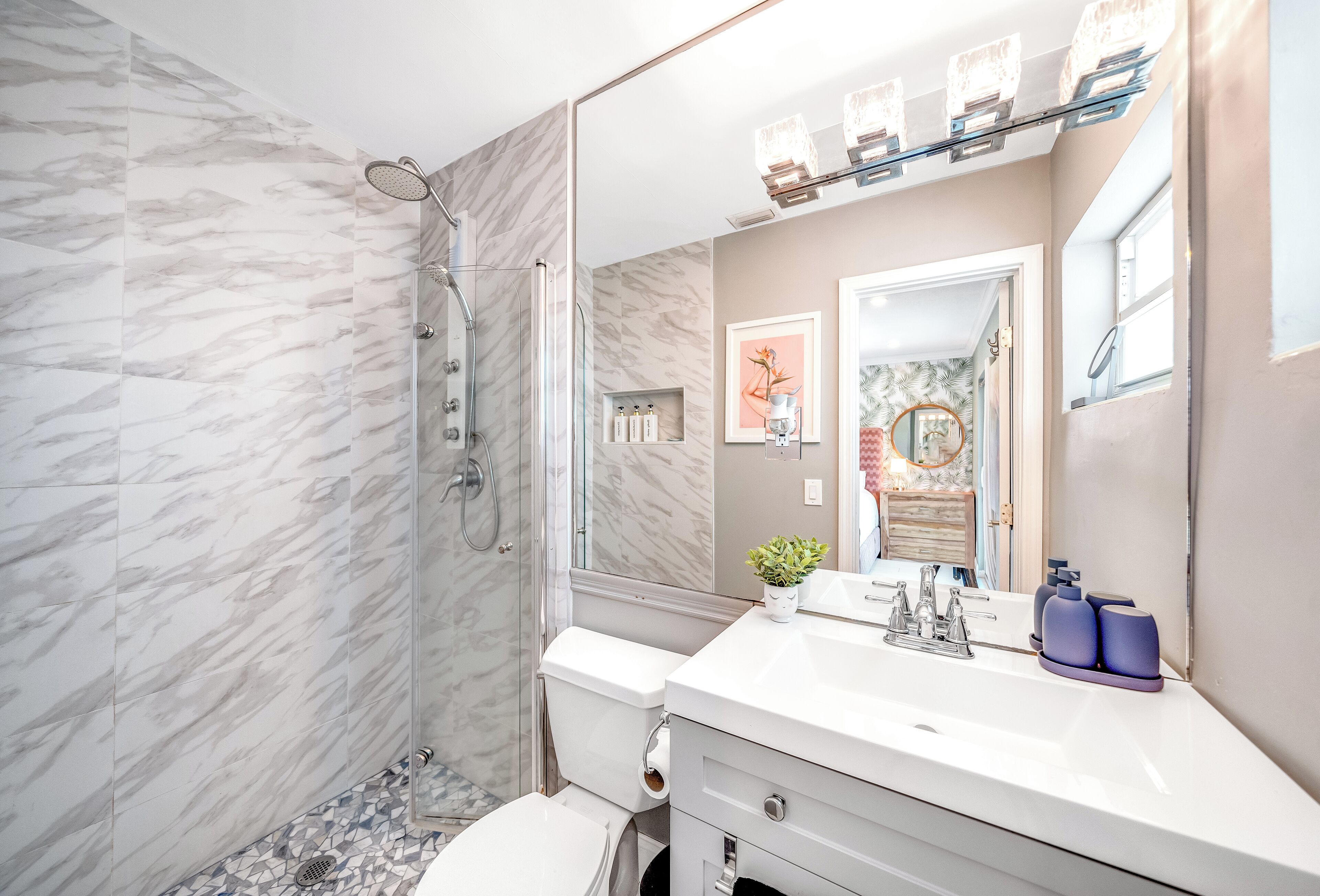 A modern bathroom with a glass-enclosed shower, a white sink with a mirror, and a marble-tiled floor.