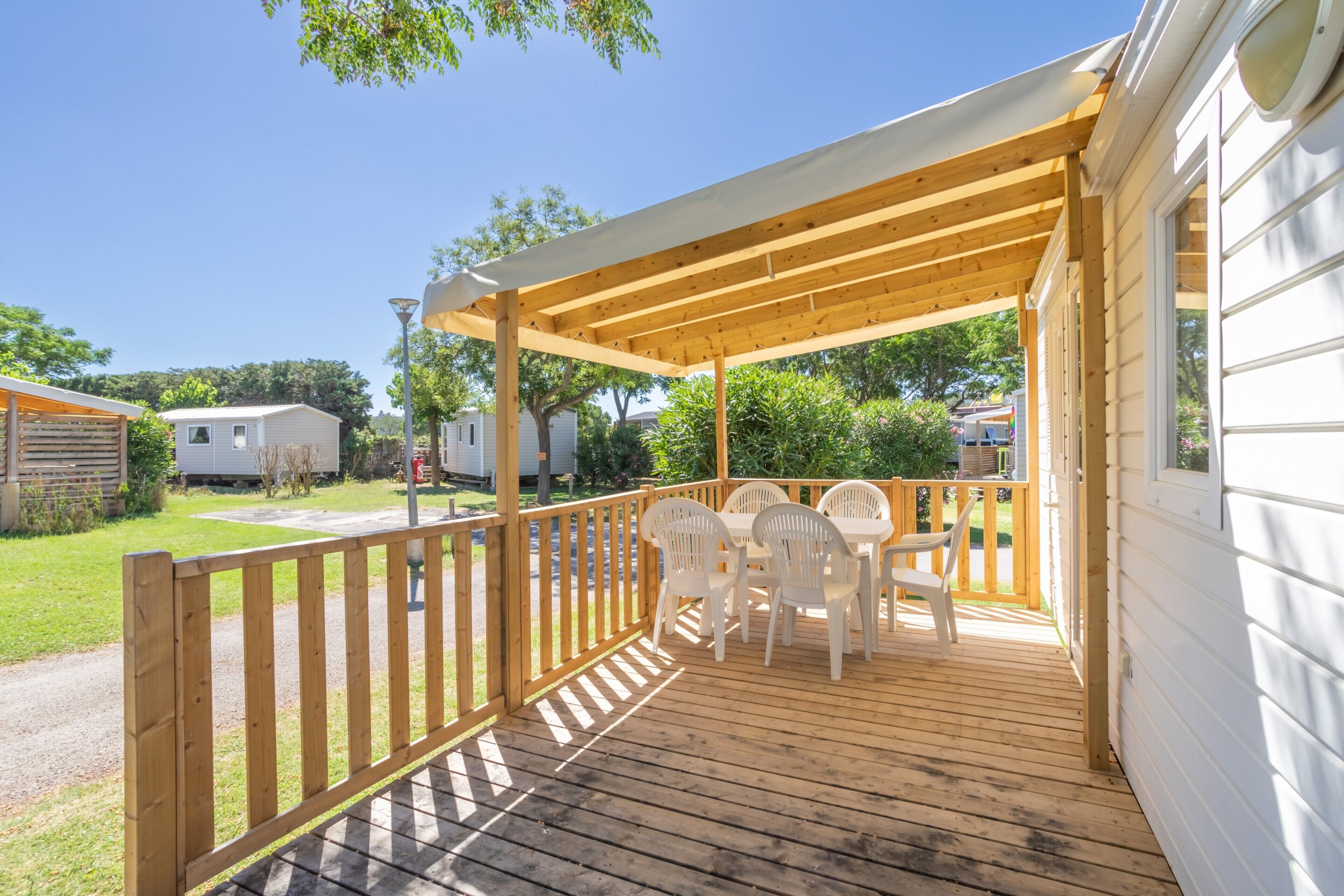 A covered outdoor deck with wooden chairs and a table, surrounded by a wooden railing.