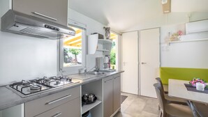 Eine moderne Küche mit Gasherd, Spüle und Schränken, ein Essbereich mit Tisch und Stühlen sowie ein Blick ins Freie.