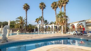 Ein Swimmingpool mit Palmen, einer Skulptur eines Seepferdchens und einer überdachten Sitzgelegenheit.