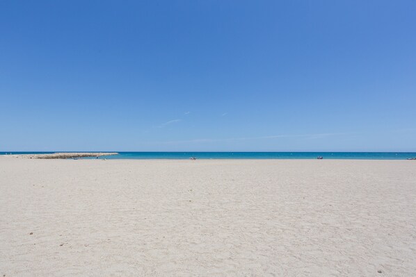 A beach with a clear sky, sandy shore, and a few people in the distance.