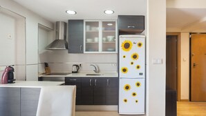 A compact kitchen with dark cabinets, a white refrigerator with sunflower decals, a sink, and a stove. - Apartment 'La Paz De Xinxilla' with Sea Views, Wi-Fi and Air Conditioning (Dénia)