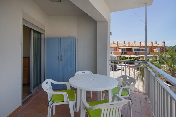 Un balcon avec une table et des chaises blanches, un meuble bleu et une vue sur un immeuble d’habitation.