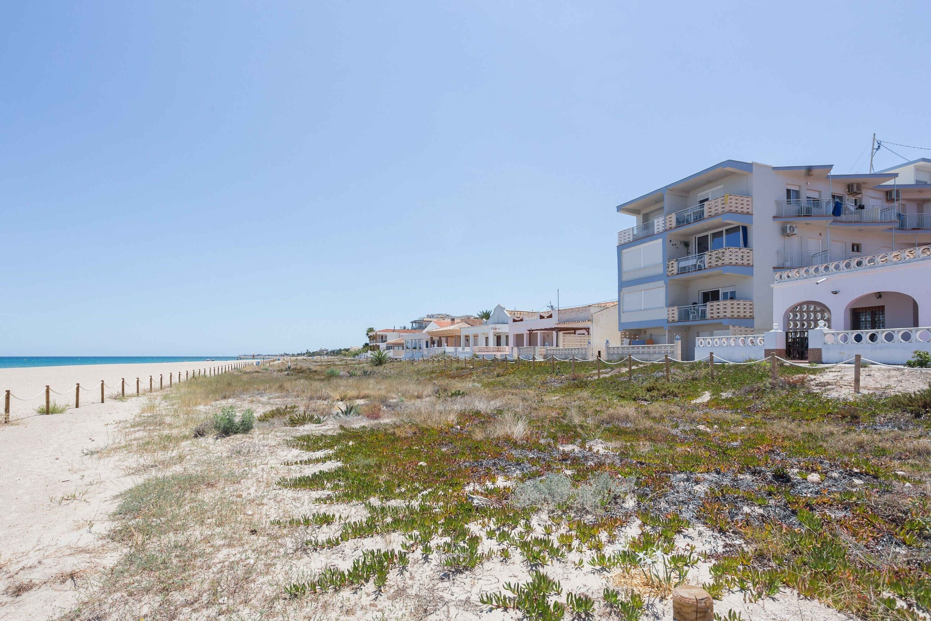 A beachfront property with multiple balconies, a sandy beach, and a clear sky.