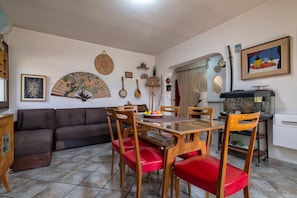 A dining area with a wooden table and chairs, a sofa, and various wall decorations including a fan and musical instruments.