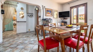 Un coin repas avec une table en bois, des chaises rembourrées de couleur rouge, un téléviseur et une fenêtre donnant sur des immeubles.