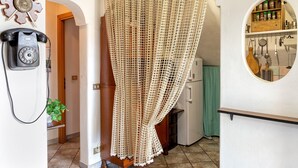 Une pièce avec un téléphone ancien, un rideau en crochet, une étagère en bois contenant des ustensiles de cuisine et un rideau à carreaux verts.