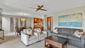 A modern living room with a grey sofa, two armchairs, a coffee table, and a dining area with a table and chairs.