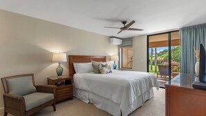 A hotel room with a bed, a chair, a nightstand, a lamp, a ceiling fan, and a view of the outdoors.