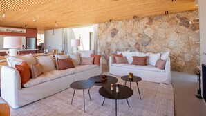 A modern living room with a wooden ceiling, stone wall, and white sofas with cushions. - Villa Lucia Di Arinella (Zonza)
