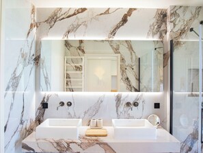 A modern bathroom with two sinks, a large mirror, and marble walls.