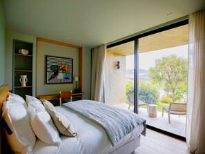 A bedroom with a large bed, a desk, a chair, a bookshelf, and a view of the outdoors.