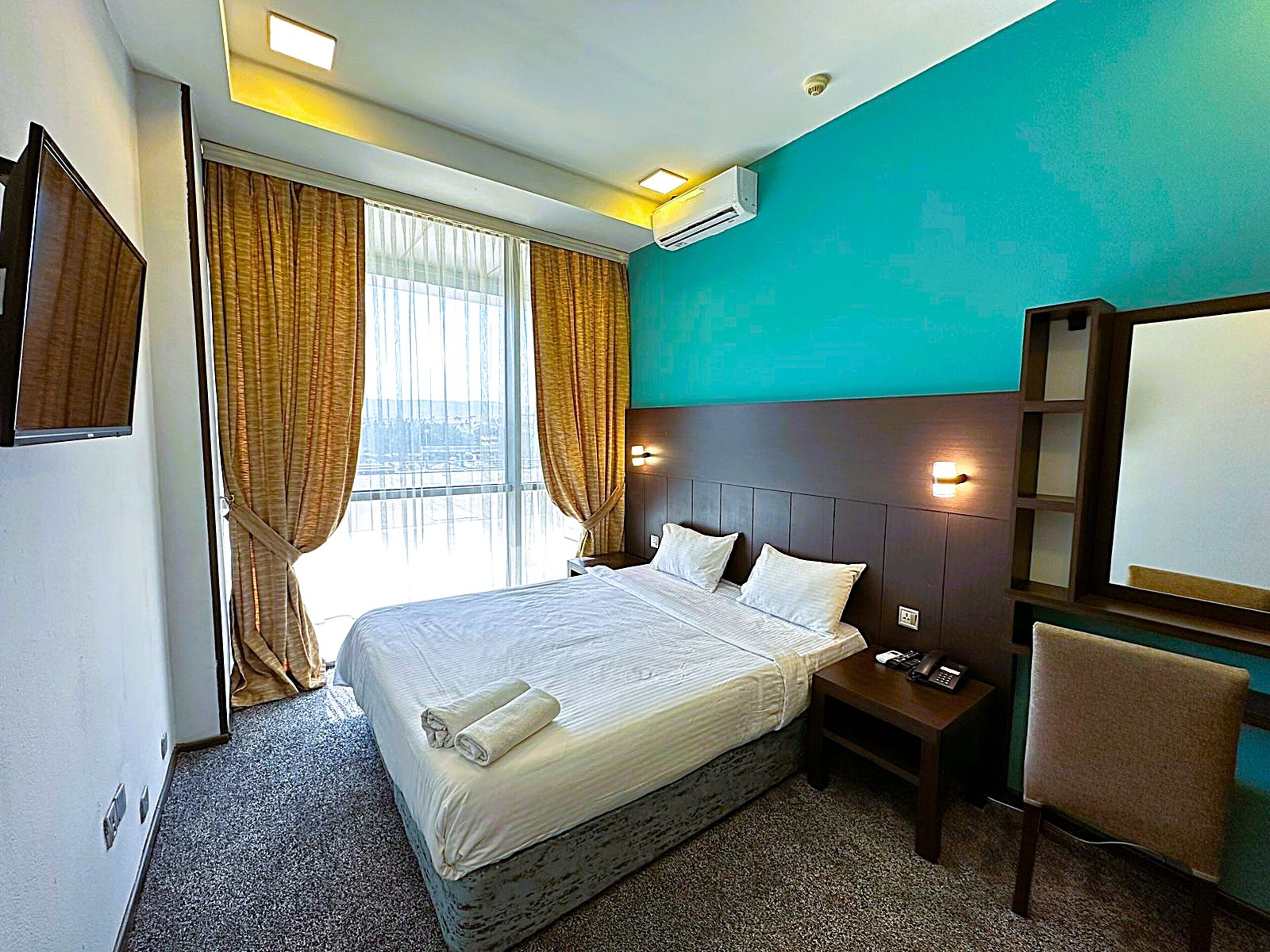 A hotel room with a large bed, a nightstand, a chair, and a view of the city through the window.