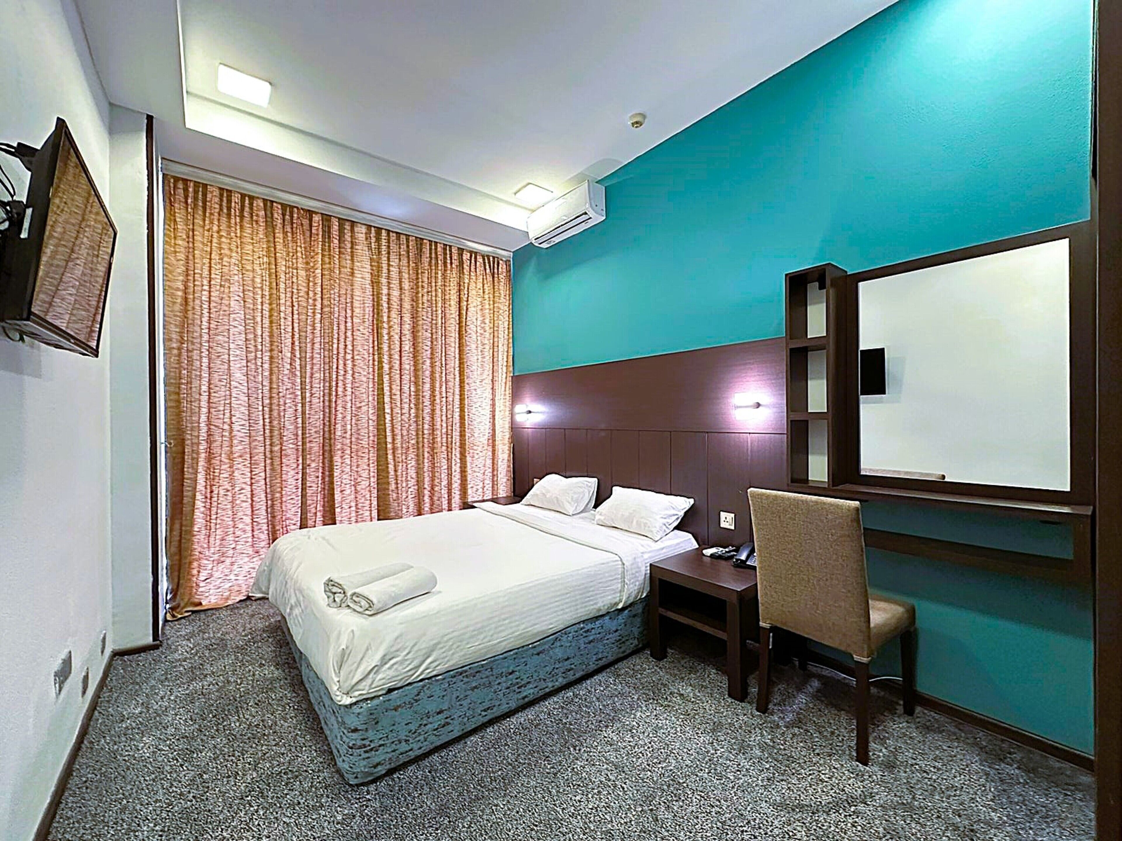 A hotel room with a bed, a desk, a chair, a TV, and a large mirror.