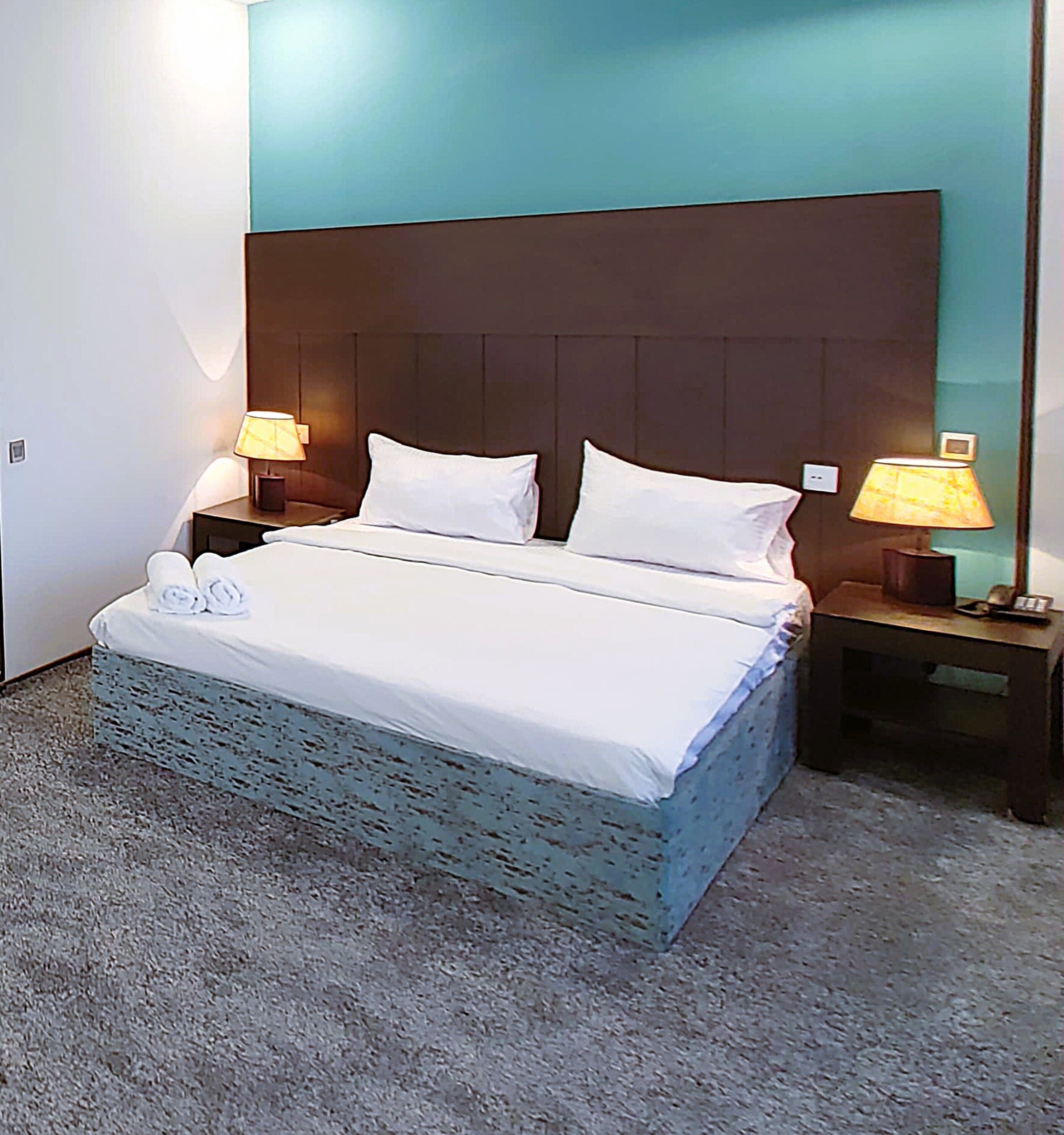 A neatly made bed with white linens, two pillows, and a small bedside table with a lamp.