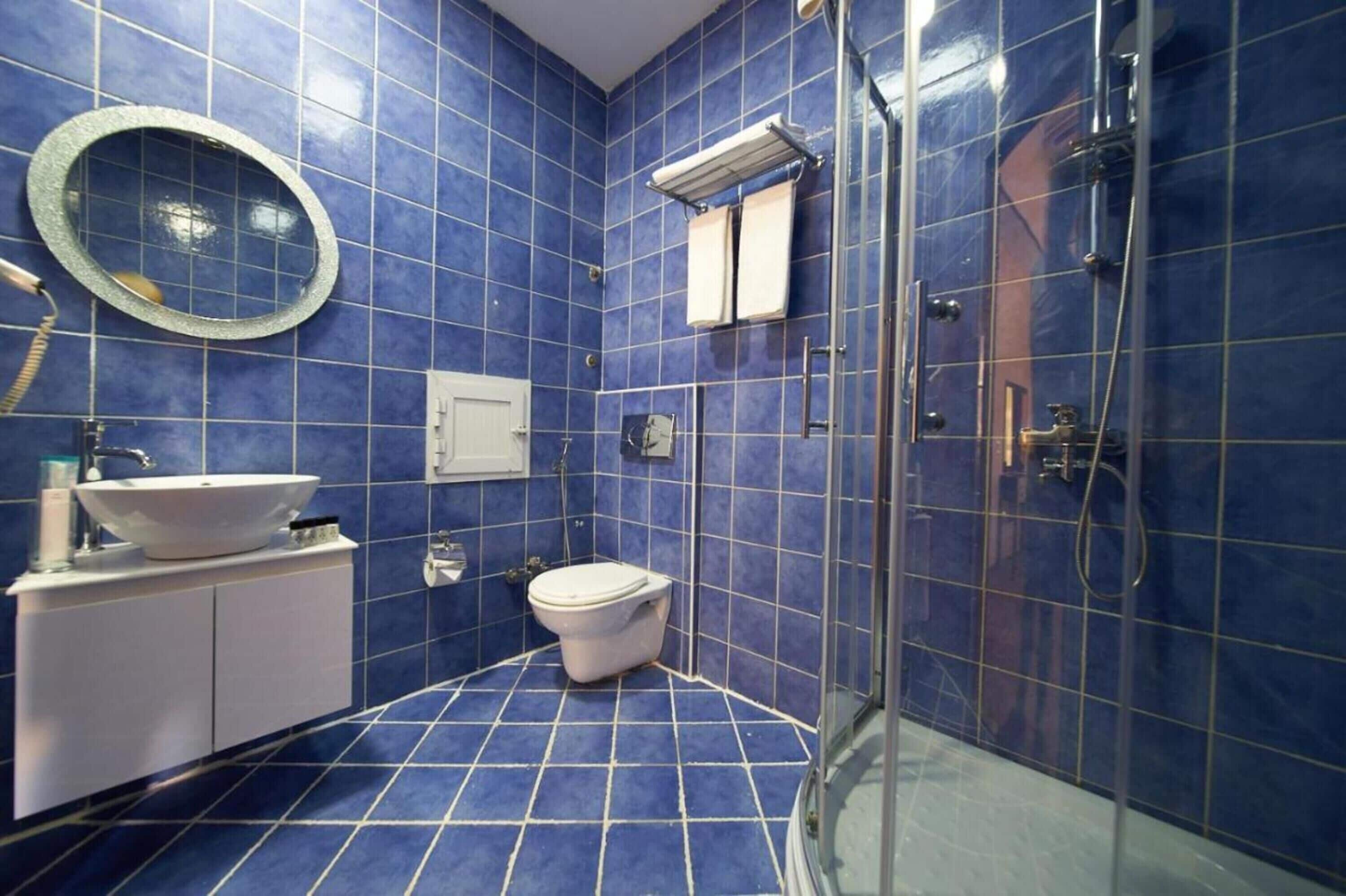 Une salle de bain avec des carreaux bleus, un lavabo blanc, des toilettes, une douche en verre et un miroir.