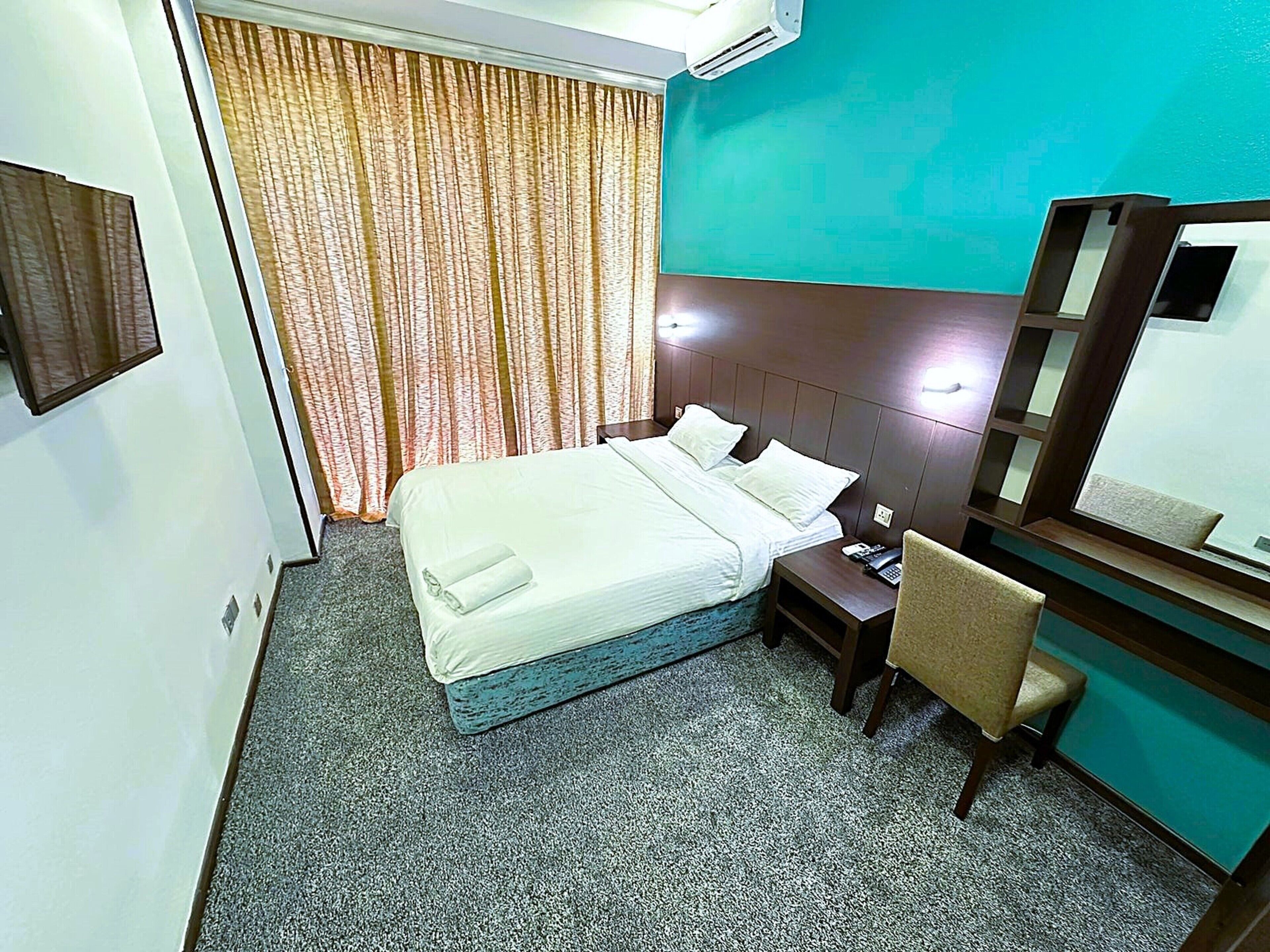 A hotel room with a bed, a desk, a chair, a telephone, and a mirror.