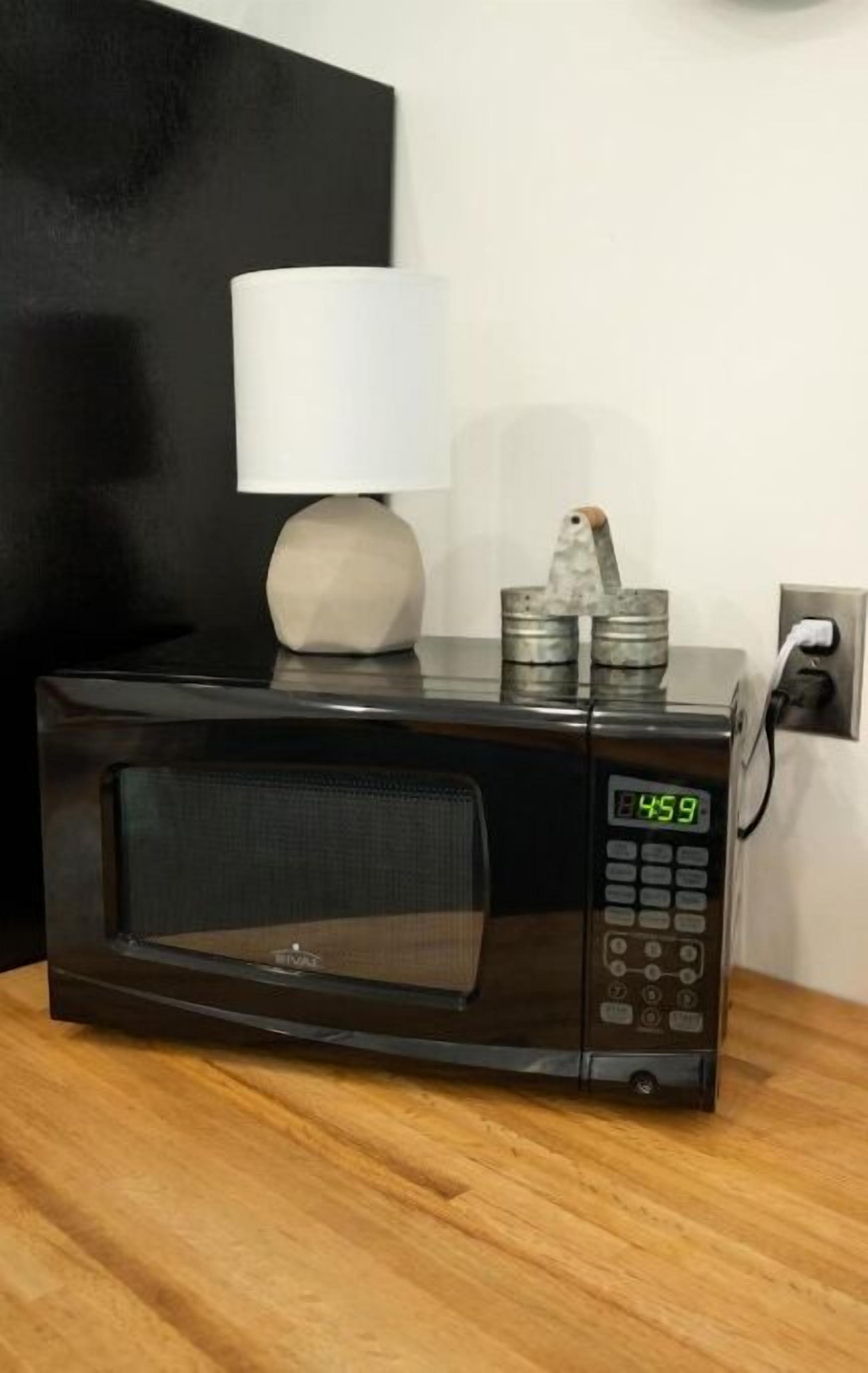 A black microwave oven with a digital display showing 4:59, a white lamp, and a metal container on top.