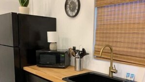 A compact kitchen with a black refrigerator, a microwave, a sink, and a window with blinds. - Hummingbird Hideaway- private self-check -Wi-Fi (Murfreesboro)