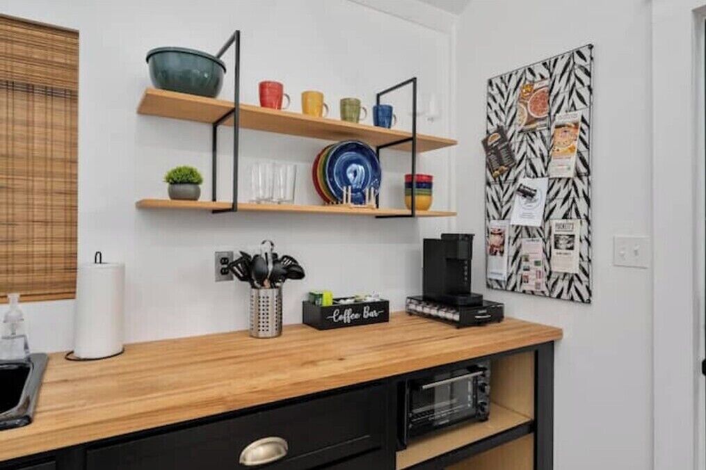 Une cuisine avec des étagères en bois où sont rangées la vaisselle et les tasses, un coin café et un tableau d’affichage où sont accrochées des notes.