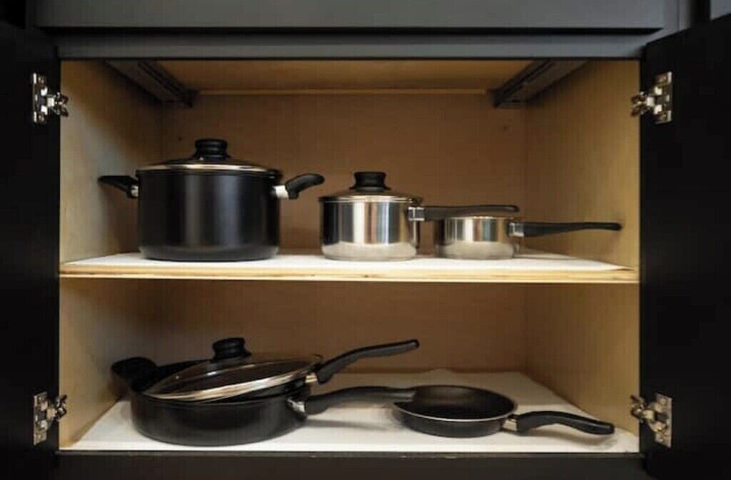 Een keukenkastje met drie planken, elk met verschillend keukengerei: een grote pan, een kleinere pan en een koekenpan.