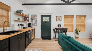 A modern kitchen with black cabinets, a wooden countertop, and a green door. There is a dining area with a table and chairs, and a green sofa. - Hummingbird Hideaway- private self-check -Wi-Fi (Murfreesboro)