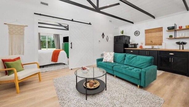 A modern living room with a green sofa, a round coffee table, and a kitchen area with black cabinets and a wooden countertop. - Hummingbird Hideaway- private self-check -Wi-Fi (Murfreesboro)