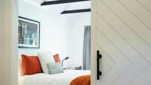 A bedroom with a bed, a white door with a chevron pattern, and a view of another room through a sliding door. - Hummingbird Hideaway- private self-check -Wi-Fi (Murfreesboro)