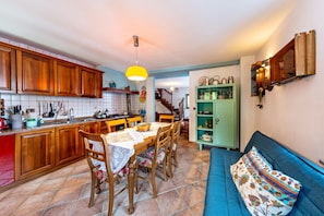 Una cocina con armarios de madera, una mesa de comedor con sillas, un sofá azul y un mueble verde con frascos.