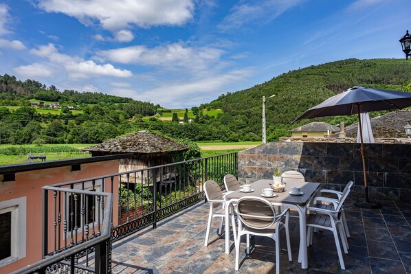 A terrace with a table and chairs, a view of a green valley, and a stone wall.