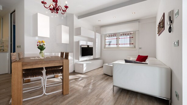 A modern living room with a dining area, a white sofa, a TV, and a chandelier.