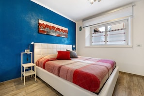 A bedroom with a bed, a nightstand, a painting on the wall, and a window.