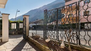 A gated entrance with a metal fence, a paved pathway, and a building with a balcony.