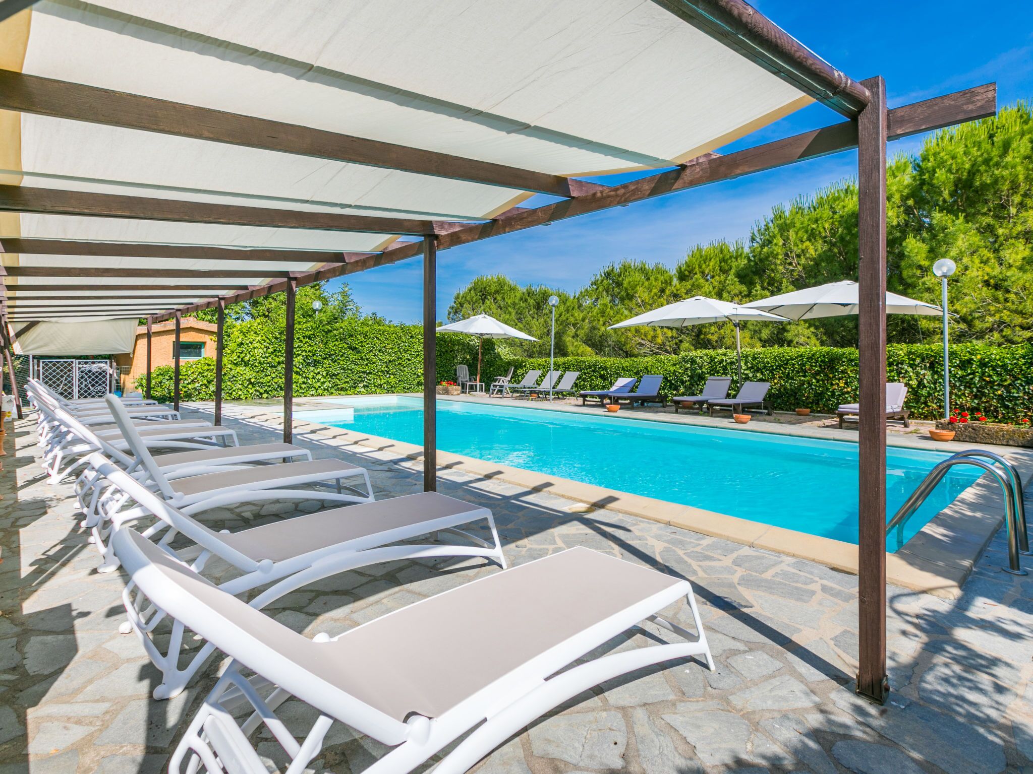 A poolside area with lounge chairs and umbrellas, a clear blue pool, and a stone-tiled deck.