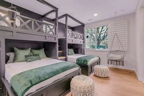 Une chambre avec des lits superposés, un fauteuil suspendu et une fenêtre avec des stores.