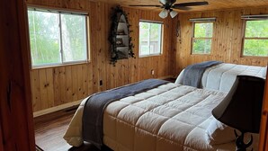 A wooden-paneled bedroom with a bed, a ceiling fan, and windows. - Heaven on Lake Edward  (Nisswa)
