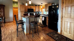 A kitchen with wooden cabinets, a black refrigerator, and a bar area with stools. - Heaven on Lake Edward  (Nisswa)