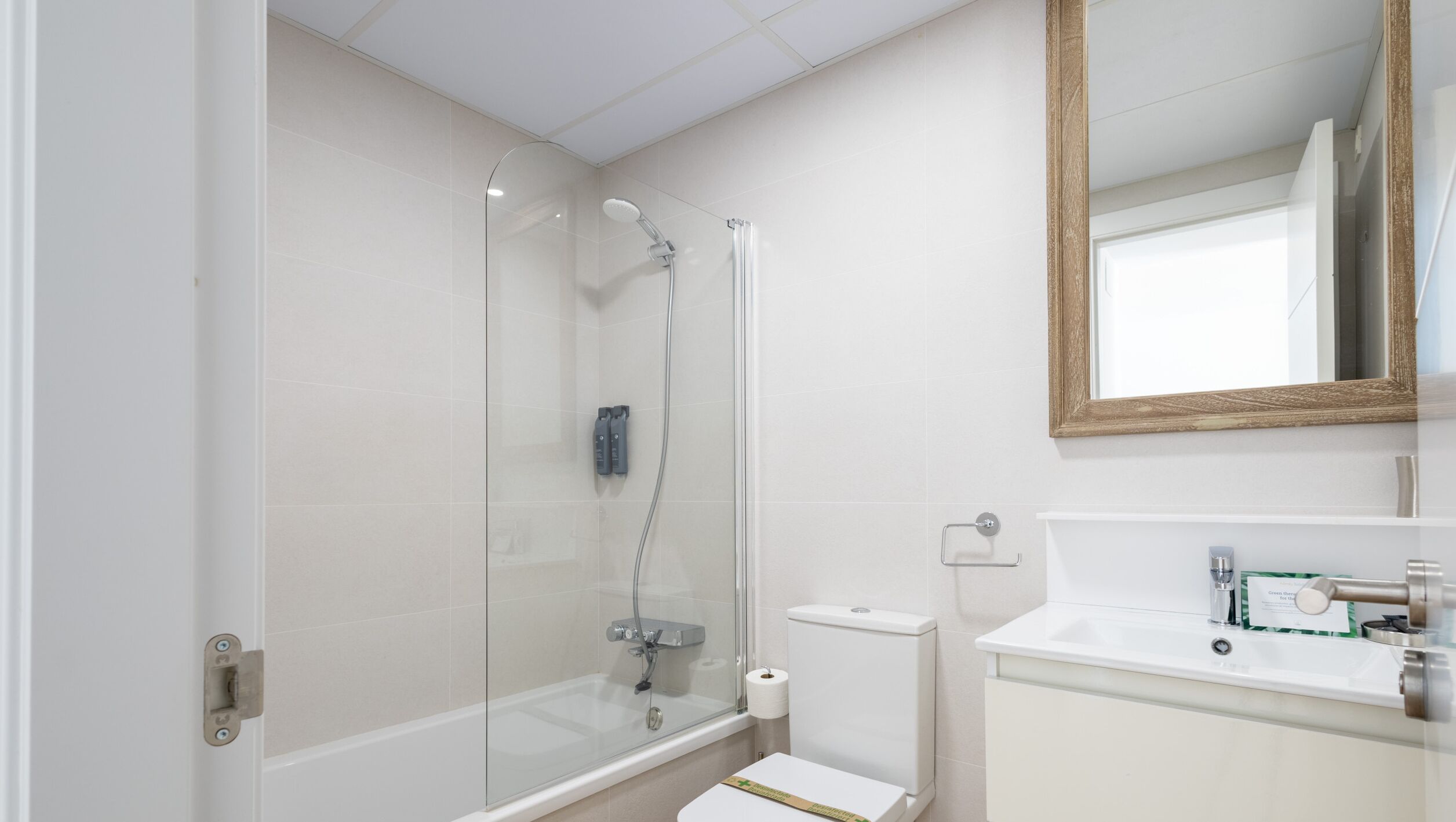 A modern bathroom with a glass-enclosed shower, a toilet, and a sink with a mirror above.