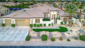 A two-story house with a garage, a front yard with a lawn and decorative rocks, and palm trees. - Walk to Stagecoach,incredible gameroom, putting green, bocce, slide, pickleball (Indio)