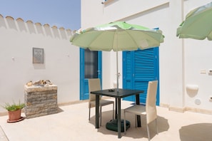 A patio with a table and chairs, a green umbrella, a stone planter, and blue doors.