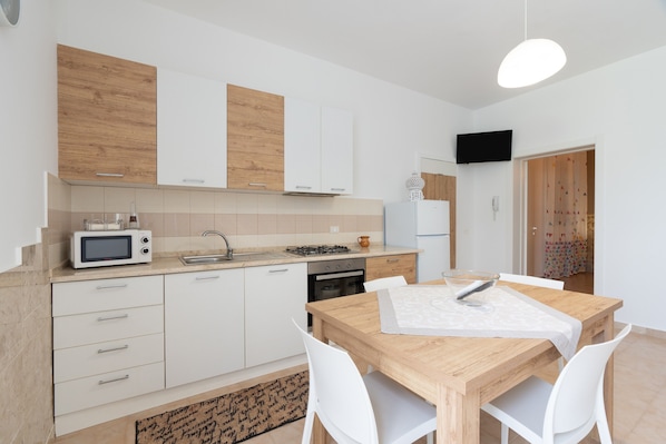 A modern kitchen with white cabinets, a microwave, a stove, and a dining table with chairs.