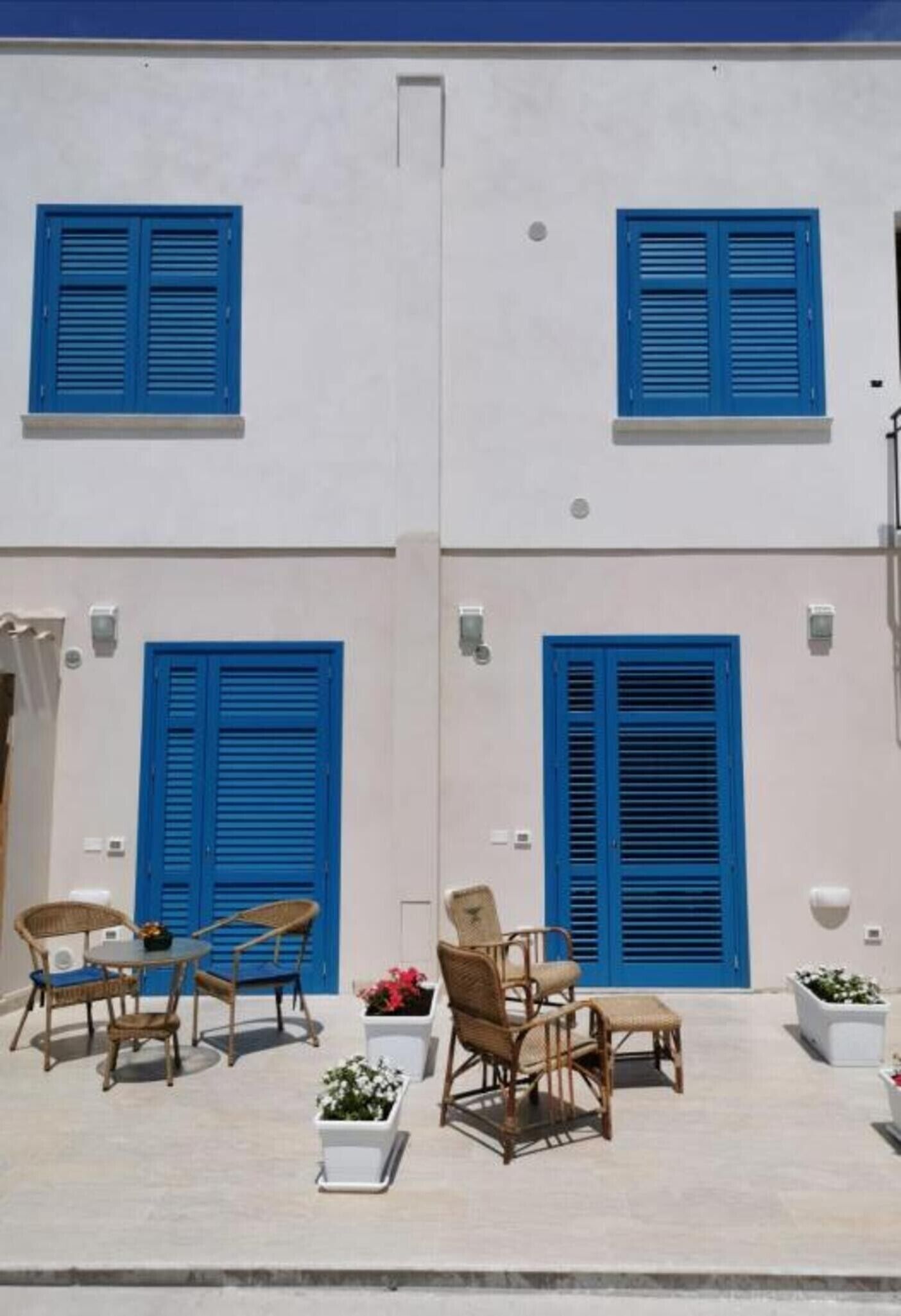 A two-story building with blue shutters, wicker furniture, and potted plants.