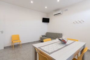 Een moderne kamer met een eettafel, stoelen, een bank, een televisie en een airconditioning.