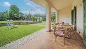 Un patio coperto con tavolo e sedie, un prato verde e vista sul paesaggio circostante.