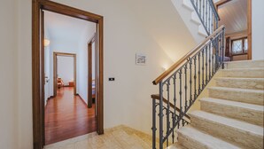 Una scala con gradini in pietra e ringhiera in ferro battuto, che conduce a una stanza con una porta in legno e un quadro appeso al muro.